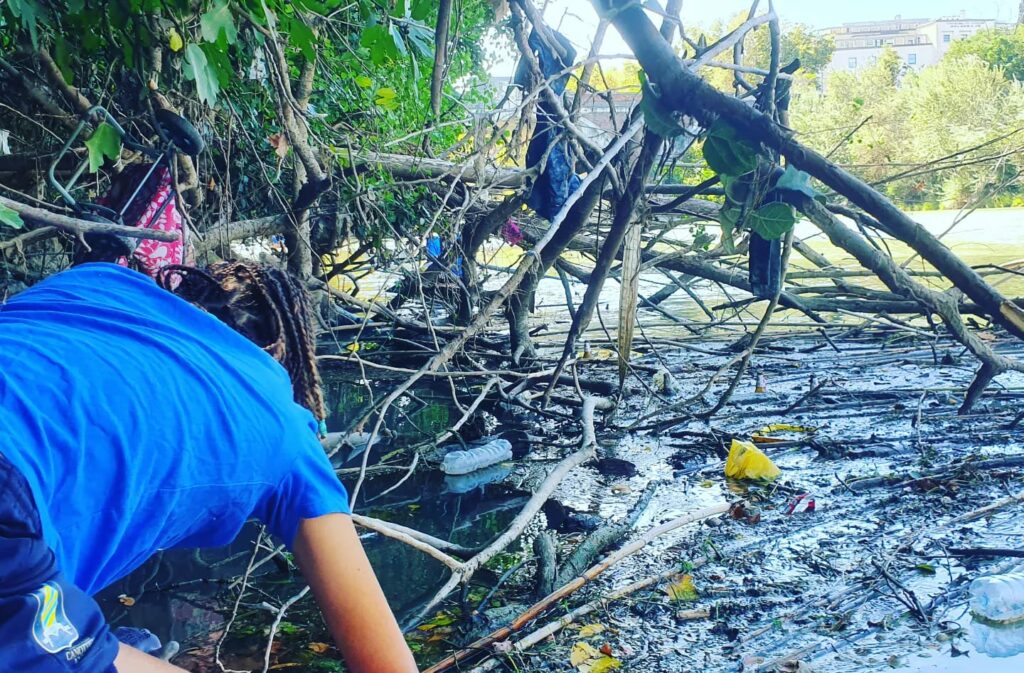 Una giovane volontaria della campagna di pulizia del Tevere, organizzata da Basiliotti, azienda leader nel packaging sostenibile, raccoglie rifiuti plastici lungo le rive del fiume. L'iniziativa mira a promuovere la sostenibilità ambientale e a ridurre l'inquinamento plastico nei corsi d'acqua.
